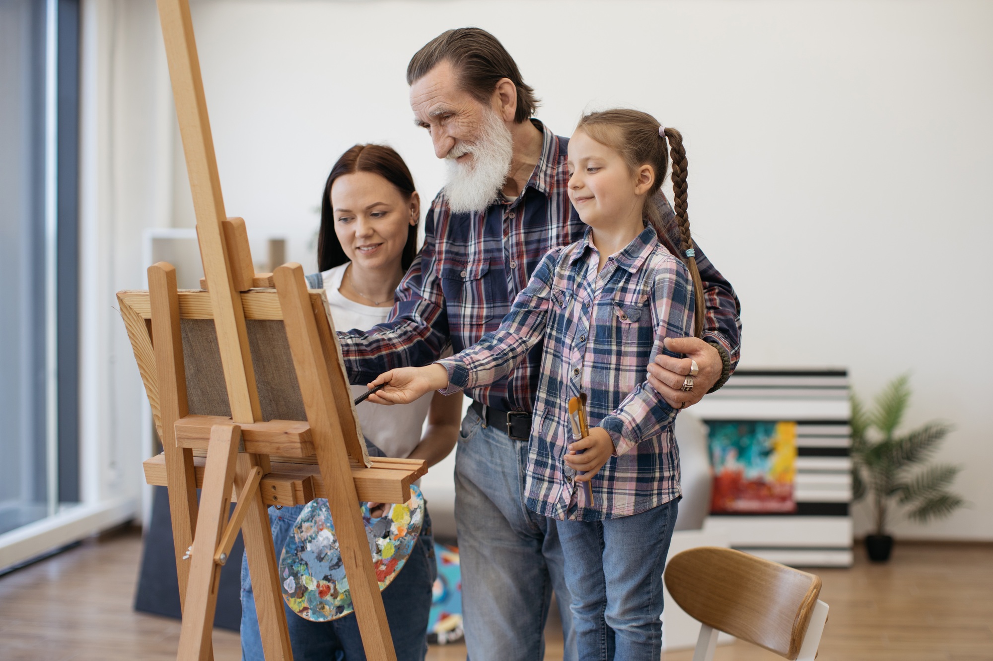 Woman and daughter peering at granddad's sketch on easel